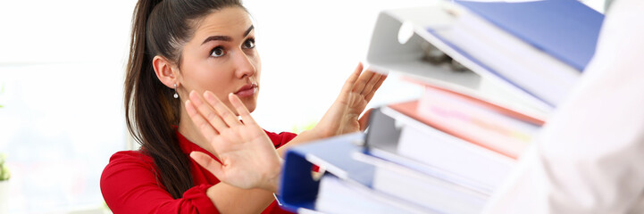 Young happy woman sitting in office and refusing to work with heap of documents