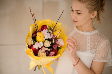 Girl holding a spring bouquet of different flowers decorated with willow branches, little chiken toy wrapped in yellow paper