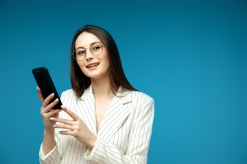 Naklejka premium Young beautiful woman using mobile phone studio on blue color background