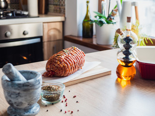 Raw turkey meatloaf on table. Uncooked spicy pork meat roulade prepared to roast, marinated with spices and herbs on a wooden plate. Olive oil in glass bottle.