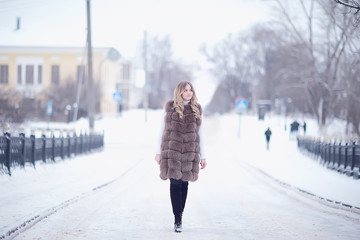 girl in a fur vest walks in the winter outside / adult young model in winter clothes fur