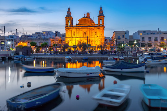 Valletta harbour with yachts and fishing boats, Msida Parish Church of Saint Joseph at sunset, Malta