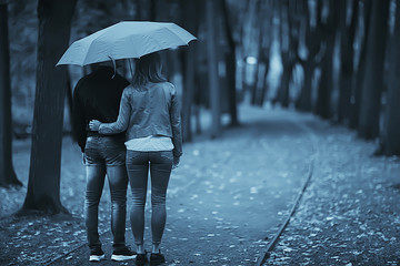 rain in the autumn park / young 25 years old couple man and woman walk under an umbrella in wet rainy weather, walk October lovers