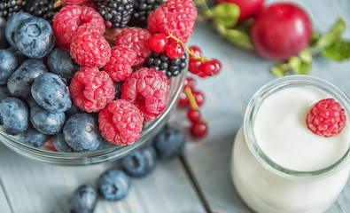 Different types of ripe berries - blueberries, raspberries, red currants, mulberries, a drink from berries and waffles with cheese. Appetizing snack with berries. Jars of natural yogurt.