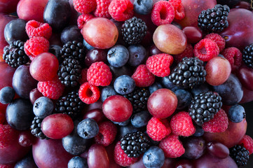 Background of fresh vegetables and fruits. Ripe blackberries, blueberries, plums, pink grapes, raspberries. Mix berries and fruits. Top view. Background berries and fruits. Black-blue and red food.