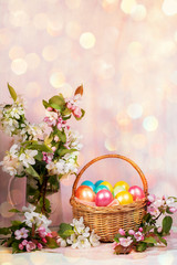 Fototapeta na wymiar Easter composition of basket of painted Easter eggs, Apple tree twigs with background with hexagonal bokeh. Vertical.