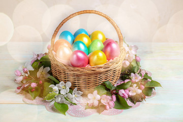 Easter composition of basket of painted Easter eggs and sprigs Apple trees around it on wooden backdrop with bokeh.