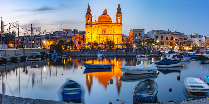 Panorama of Valletta harbour with yachts and fishing boats, Msida Parish Church of Saint Joseph at sunset, Malta