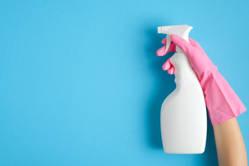 Female hand in pink glove holding cleaning spray bottle on blue background. House cleaning or...