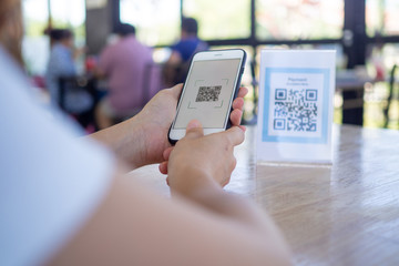 Women's hand uses a mobile phone application to scan QR codes in stores that accept digital payments without money and plastic tags on the table. QR code payment and cash technology concept