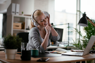 Portrait of businesswoman in office. Beautiful woman listening music at work.