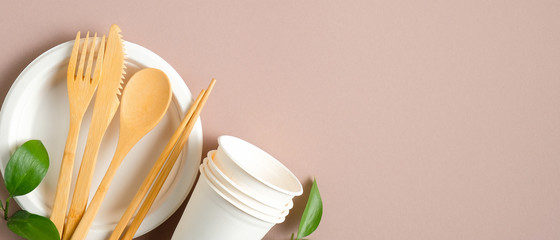 Eco store banner design. Eco-friendly wooden cutlery set, paper cups and plate with green leaves on...