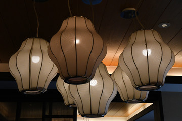 Lamp in a room. Retro lamps with geometric lampshades in shape of lanterns hanging under ceiling. Matte surface of traditional Chinese lamps with glowing light bulbs inside.
