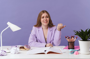 Confused woman sit at the table pointing aside.