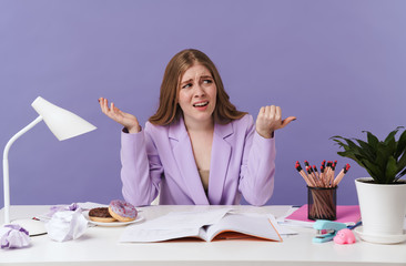 Confused woman sit at the table pointing aside.