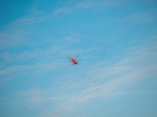 Far red helicopter in blue sky. Emergency service helicopter flight. Banner template with text place. Insurance or medical support concept. Sunny blue sky and special service flying vehicle.