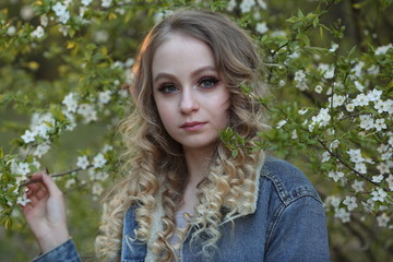 Naklejka premium beautiful blonde in a blue denim jacket in a spring garden where trees bloom, close-up