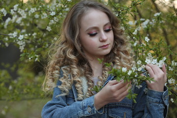 Naklejka premium beautiful blonde in a blue denim jacket in a spring garden where trees bloom, close-up