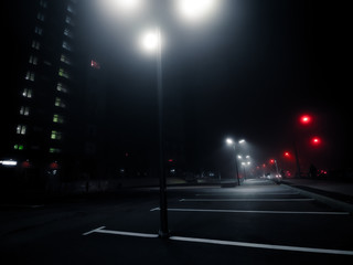 Cyberpunk style urban landscape. Empty parking with tall lamp posts near skyscraper in the night. Bottom view. Modern street lights in the fog on empty parking near residential apartment building.