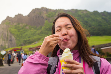 An Asia Chinese lady eat an ice cream, with background of volcanic cone in Jeju-island, Korea