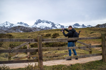 Fototapeta na wymiar young man taking a picture from a bridge with scenic views of snowed mountains and green hills behind