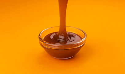 Pouring caramel sauce on color background