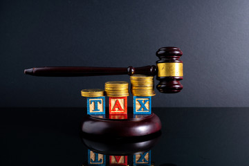 Gavel hammer and stacking coins and tax letter cube with low light view.