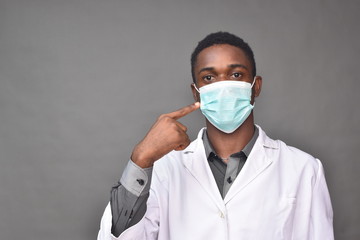 young black man wearing a white coat and face mask, indicating at wearing a face mask
