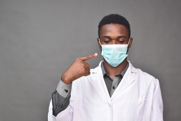 young black man wearing a white coat and face mask, indicating at wearing a face mask