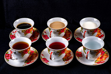 Six cups and saucers filled with water, juice, tea, coffee, milk and coffee with milk on a dark fabric background © Aleksey