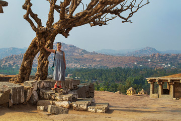 Tourist girl near an ancient building with a tree. The Group of Monuments at Hampi was the centre of the Hindu Vijayanagara Empire in Karnataka state in India