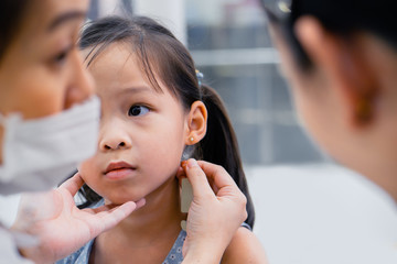 Little asian girl preparing for ear piercing process.