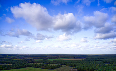 Cultural landscape of northern Germany with forests, fields and meadows under a blue and white sky with clouds
