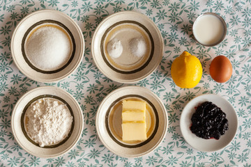 Obraz na płótnie Canvas Ingredients displayed on a decorative tablecloth for breakfast (Sugar, salt, yeast, milk, lemon, egg, flour, butter and jelly)