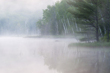 Spring landscape at dawn of Council Lake in fog with reflections in calm water, Michigan's Upper Peninsula, USA