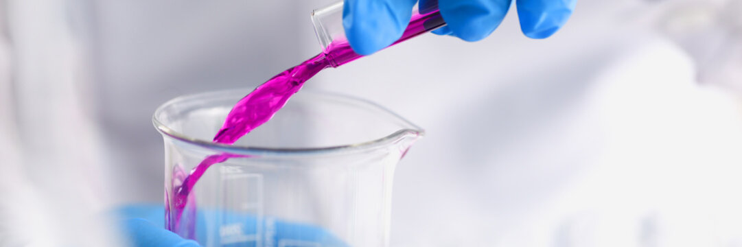 A male chemist holds test tube of glass in his hand overflows a liquid solution of potassium permanganate conducts an analysis reaction takes various versions of reagents using chemical manufacturing