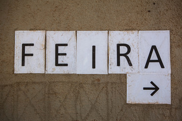 Letters printed on paper and taped to the wall with the word fair in Portuguese and an arrow.