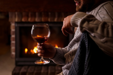 Man with glass of wine near fireplace at home, closeup - Powered by Adobe