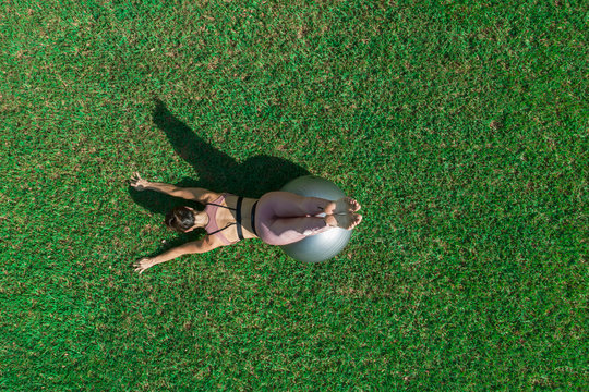 Sporty young woman doing stretching exercise with a ball in a dress field, balance posture. Beautiful athletic girl practicing yoga or pilates.