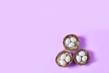 cute little white eggs lie in nests on a purple background. holiday Easter concept. flat lay, space for a text