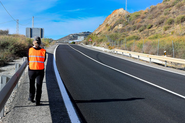 Mujer camina por la carretera con un chaleco naranja de seguridad vial