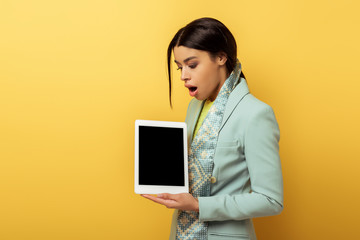 shocked african american woman holding digital tablet with blank screen on yellow