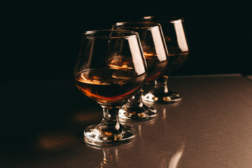 three glasses with cognac in a row on a dark background