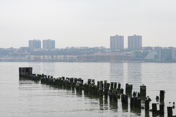 Obraz premium Wood Posts in the Hudson River along the Shore of Lincoln Square New York City with a view of West New York New Jersey during a Foggy Day