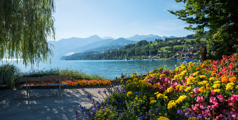pictorial lakeside promenade Faulensee, with bench and colorful flowers, view to lake Thunersee and...
