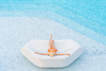Top view of Asian woman wearing sexy orange swimsuits with hat leisure and relaxing lounging on white outdoor sofa sun bed lounger at the big swimming pool. Summer vacation concept.