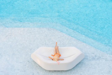 Top view of Asian woman wearing sexy orange swimsuits with hat leisure and relaxing lounging on white outdoor sofa sun bed lounger at the big swimming pool. Summer vacation concept.