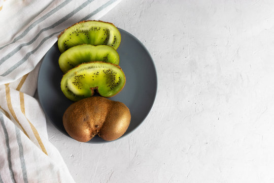 Flat lay, imperfect kiwi fruit on a gray plate with a striped napkin.
