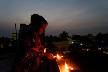 Obraz premium Young and beautiful Indian Gujarati couple in Indian traditional dress lightening Diwali diya/lamps sitting on the terrace in blue hour on Diwali evening. Indian lifestyle and Diwali celebration