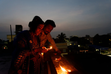 Young and beautiful Indian Gujarati couple in Indian traditional dress lightening Diwali diya/lamps sitting on the terrace in blue hour on Diwali evening. Indian lifestyle and Diwali celebration